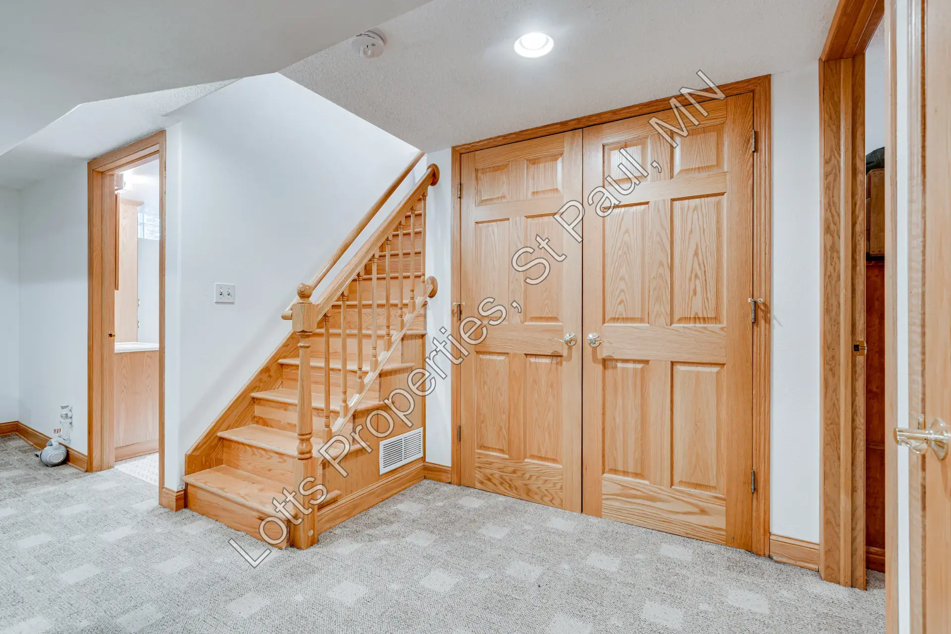 Basement stair landing with hardwood steps, closed laundry-room doors, and an open bathroom door