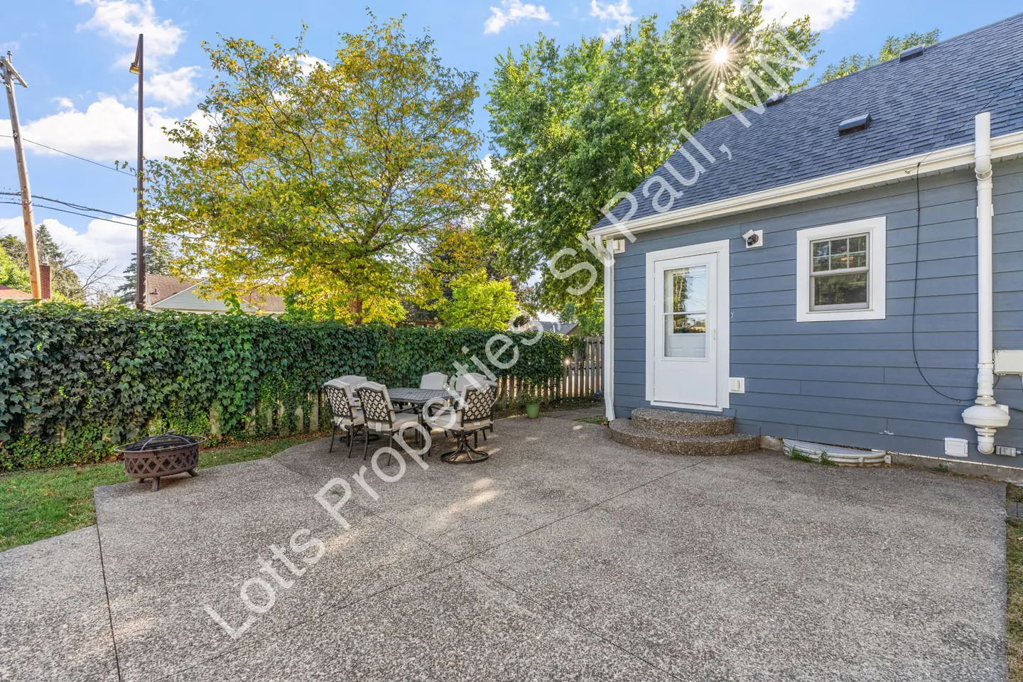 Concrete patio with outdoor dining furniture and fire pit beside the home's rear entry.