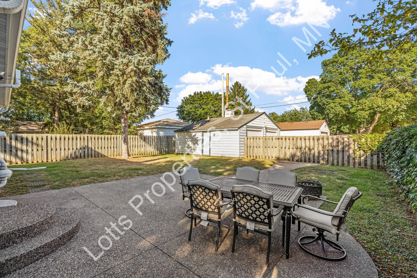 Backyard patio and lawn with patio dining set facing a detached garage behind a fence.