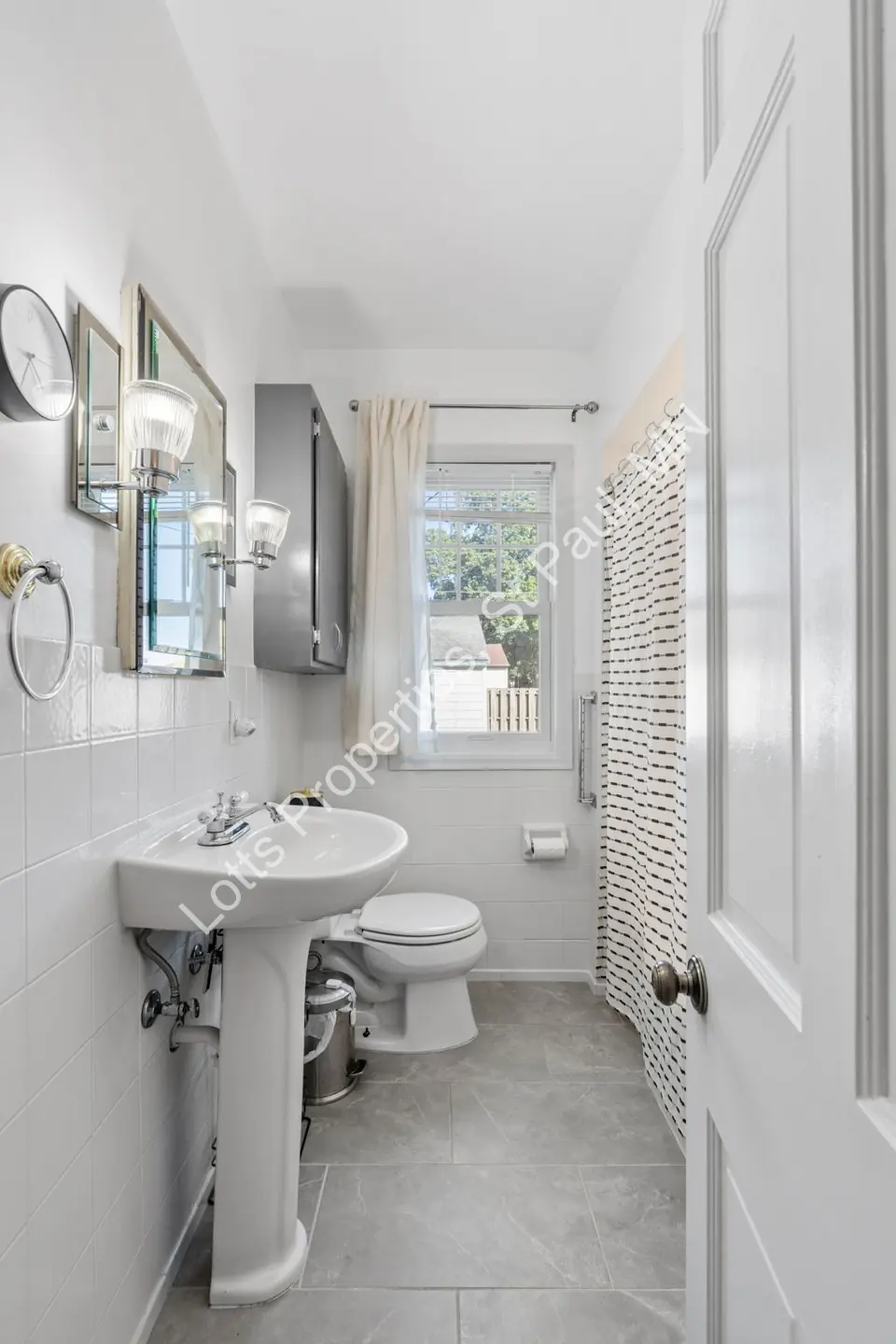 Portrait view of the bathroom with pedestal sink, mirror, and tile floor.