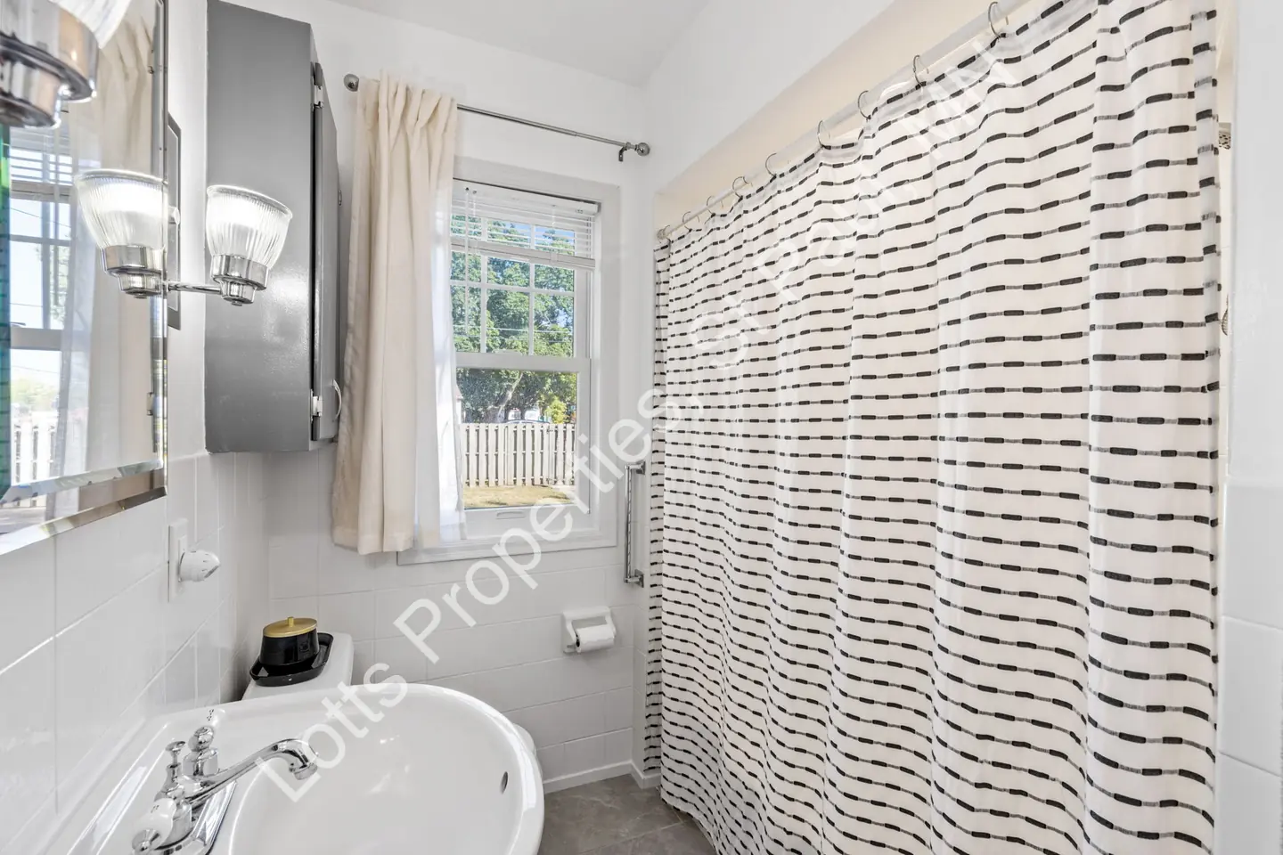 Bathroom shower with striped curtain, tiled walls, and a window letting in light.
