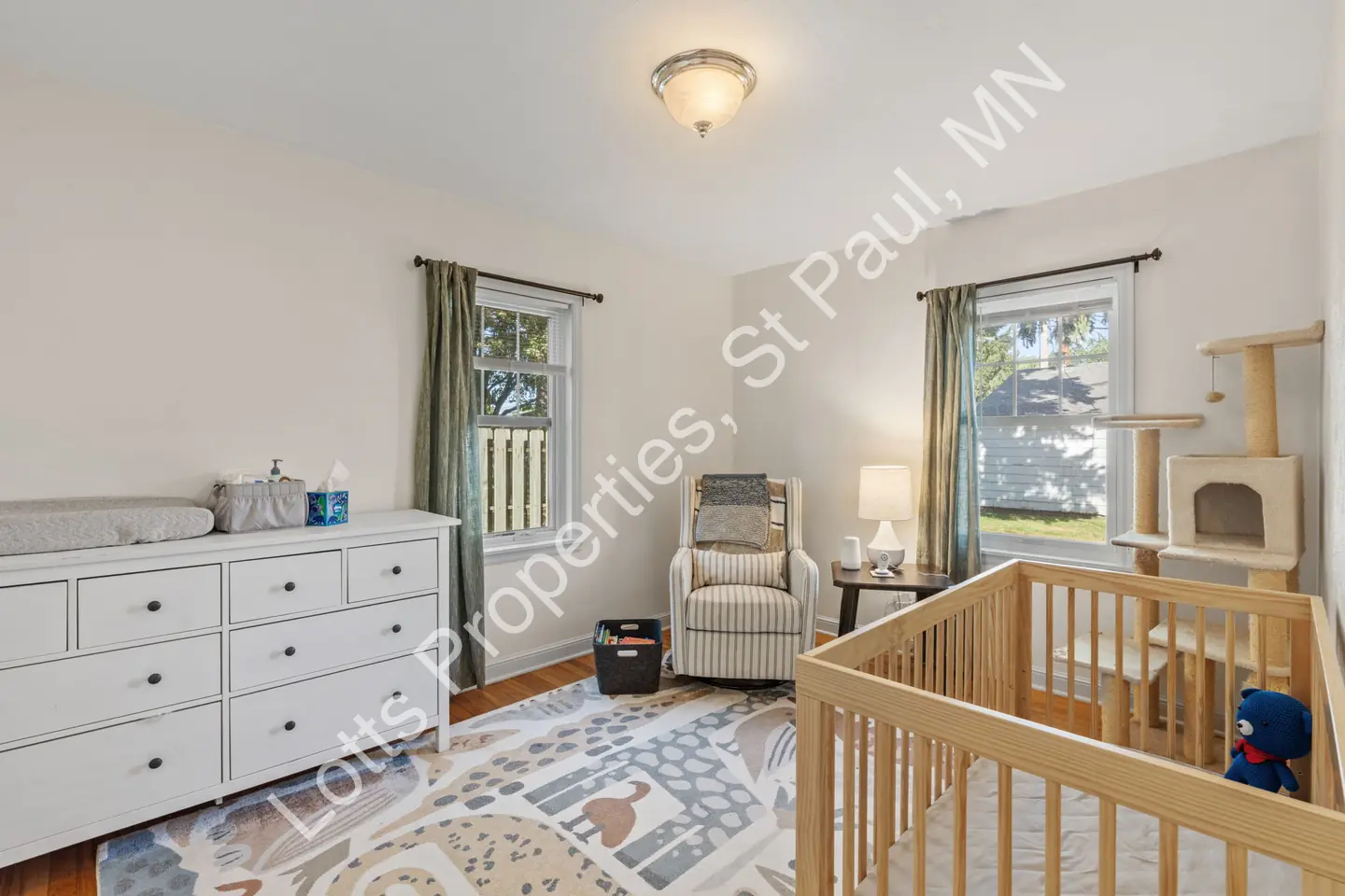 Main-floor bedroom used as a nursery with hardwood floors and two windows.
