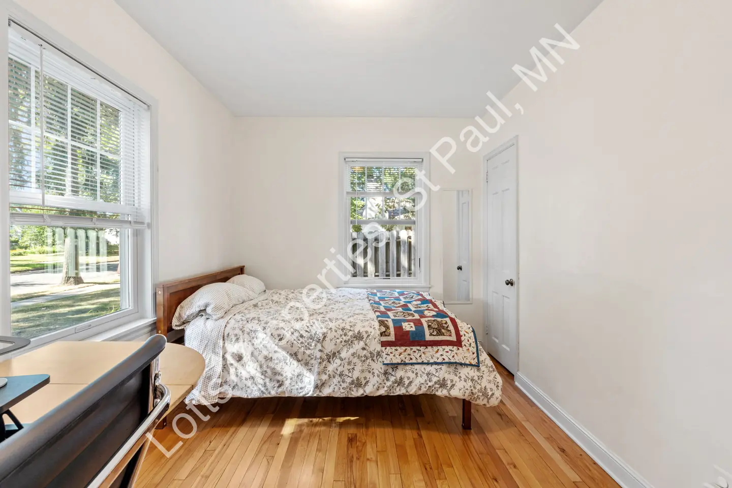 Reverse view of the bedroom with a bed beneath windows and hardwood floors.
