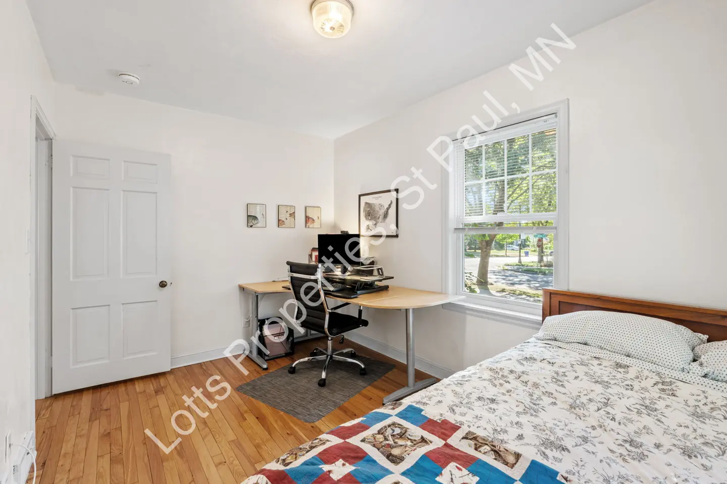 Bedroom with a desk, paneled door, and window over hardwood floors.