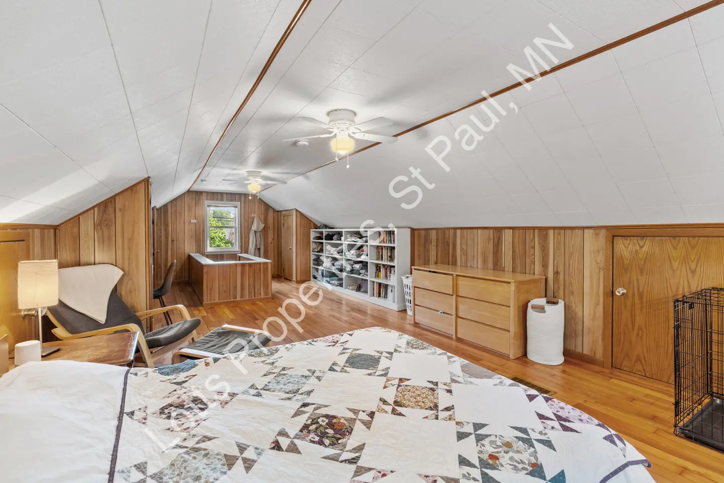 Upstairs bedroom with built-in shelves, dresser, and wood paneling under a sloped ceiling.