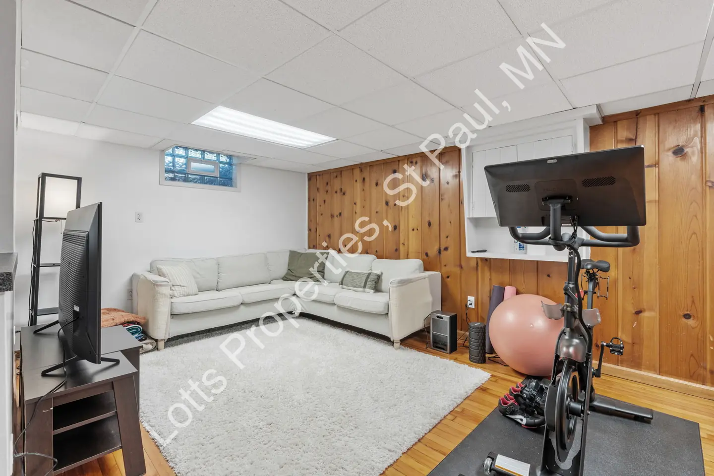 Finished basement with a sectional sofa, exercise bike, and knotty-pine wall.