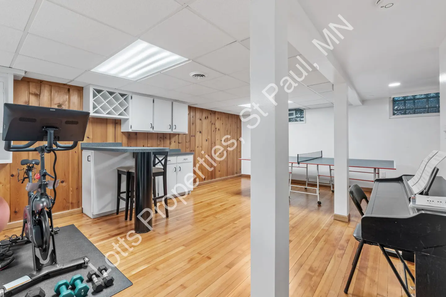 Basement bar area with white cabinets, wine rack, and high-top stools near a ping-pong table.