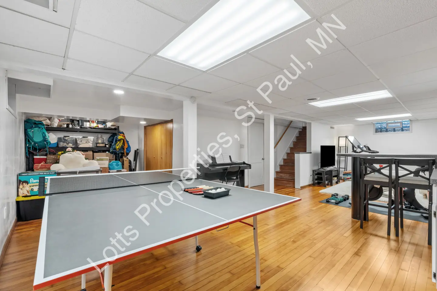 Basement game area with a ping-pong table, shelving, and staircase.