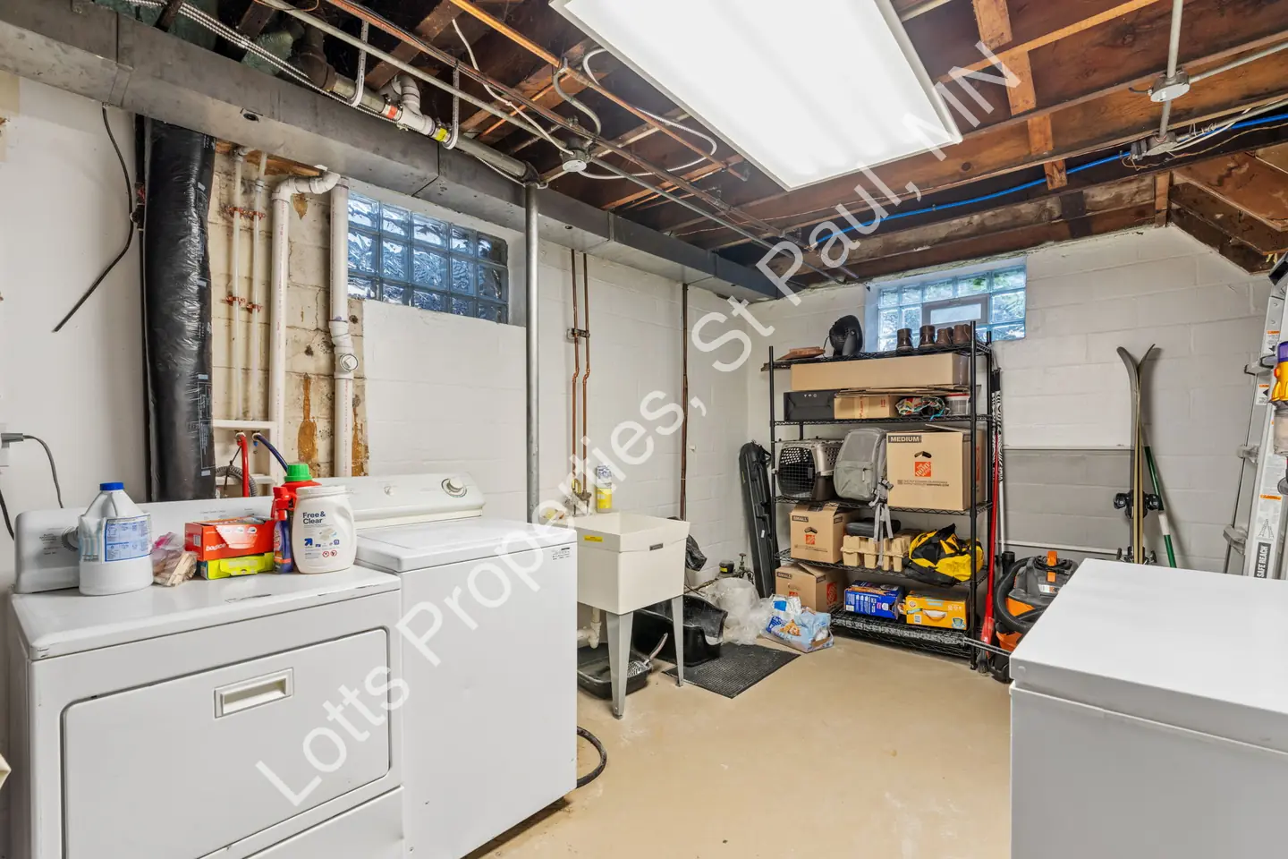 Reverse view of the utility room with laundry machines, sink, and storage shelves.